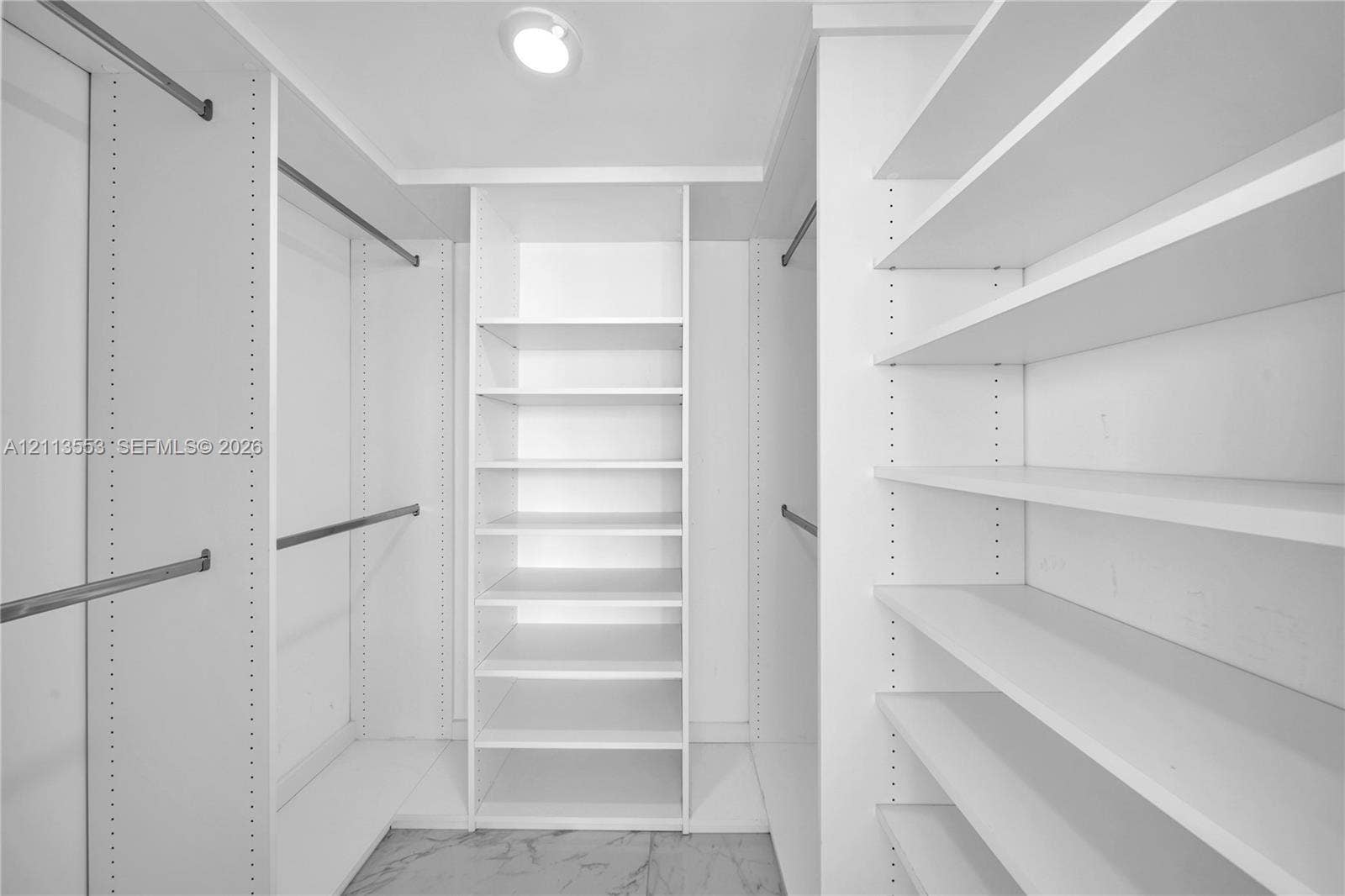 400 S Pointe Drive, #2106, Miami Beach, FL 33139 Custom walk-in closet featuring white built-in shelving, adjustable storage racks, metal garment rods, and stone-finish flooring