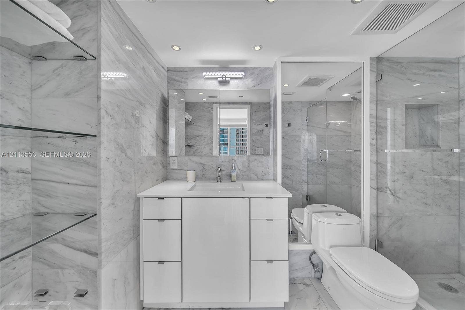 400 S Pointe Drive, #2106, Miami Beach, FL 33139 Bathroom featuring floor-to-ceiling stone-tiled walls, a white vanity with integrated basin, recessed lighting, glass shelving, and a frameless glass-enclosed shower