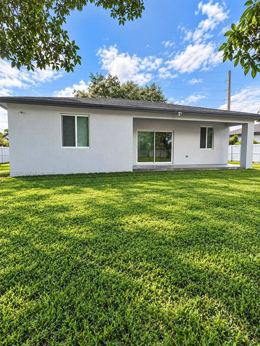 104 NW 31st Avenue, Fort Lauderdale, Fort Lauderdale, FL 33311 Rear exterior featuring a covered concrete patio, sliding glass doors, white vinyl perimeter fencing, and a manicured lawn