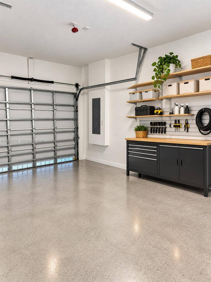 104 NW 31st Avenue, Fort Lauderdale, Fort Lauderdale, FL 33311 Finished garage featuring epoxy-coated flooring, built-in metal cabinetry with wood-finish work surface, wall-mounted organizational slat wall, and tiered wooden shelving