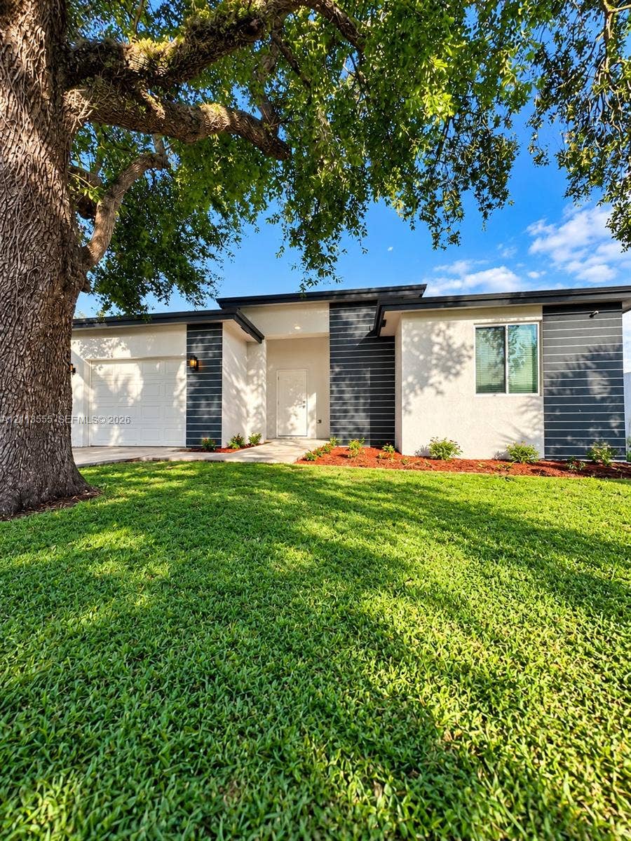 104 NW 31st Avenue, Fort Lauderdale, Fort Lauderdale, FL 33311 Single-story exterior featuring a stucco and horizontal siding facade, flat roofline, attached garage, and mature tree canopy