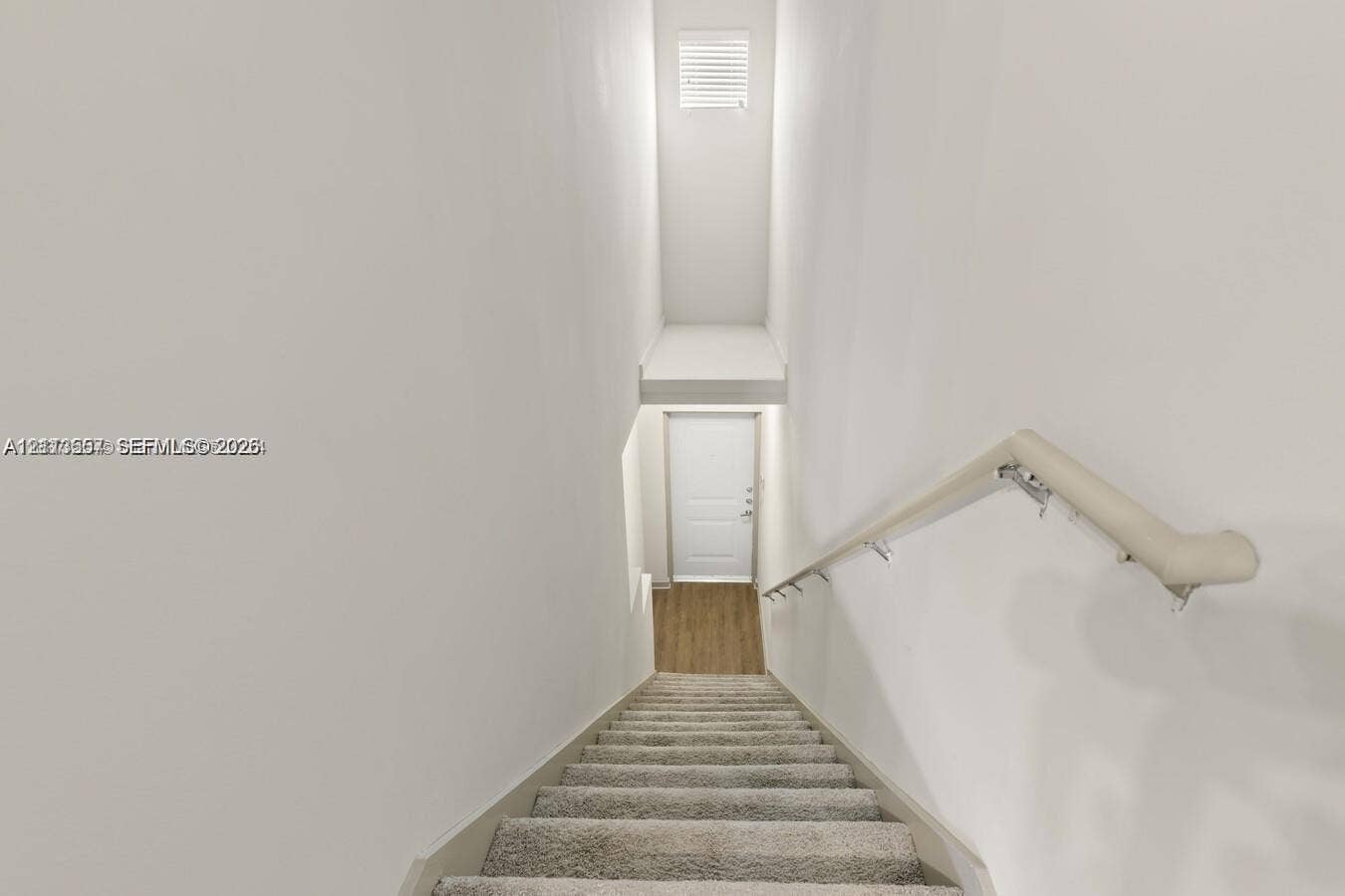 320 Franklin Club Drive, #Boca 1, Delray Beach, Delray Beach, FL 33483 Staircase featuring neutral-toned carpeting, a wall-mounted handrail, and a direct line of sight to a white interior door with wood-finish flooring