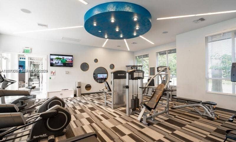 320 Franklin Club Drive, #Boca 1, Delray Beach, Delray Beach, FL 33483 Fitness center featuring a circular recessed ceiling light feature, patterned carpet flooring, large multi-shape wall mirrors, linear recessed lighting, and expansive windows with horizontal blinds
