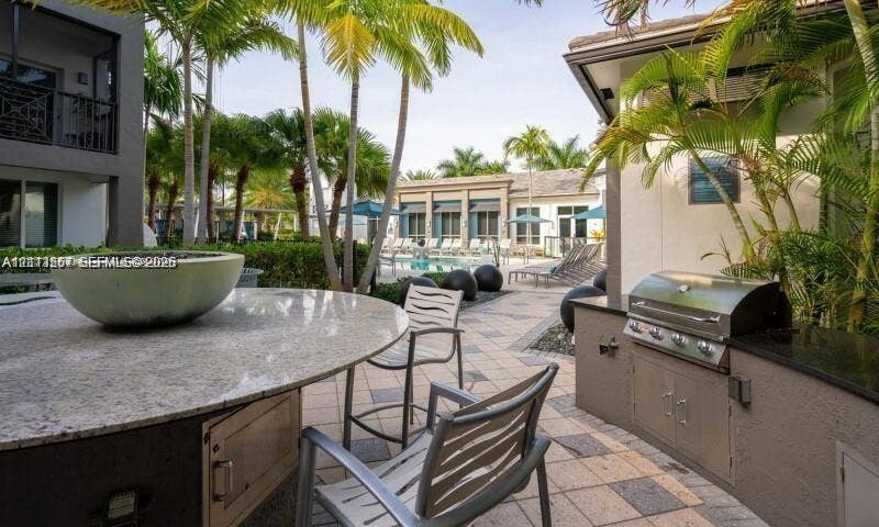320 Franklin Club Drive, #Boca 1, Delray Beach, Delray Beach, FL 33483 Outdoor kitchen area featuring a built-in stainless steel grill, stone-finish countertops, tile patio flooring, and a circular stone-topped bar with a central basin