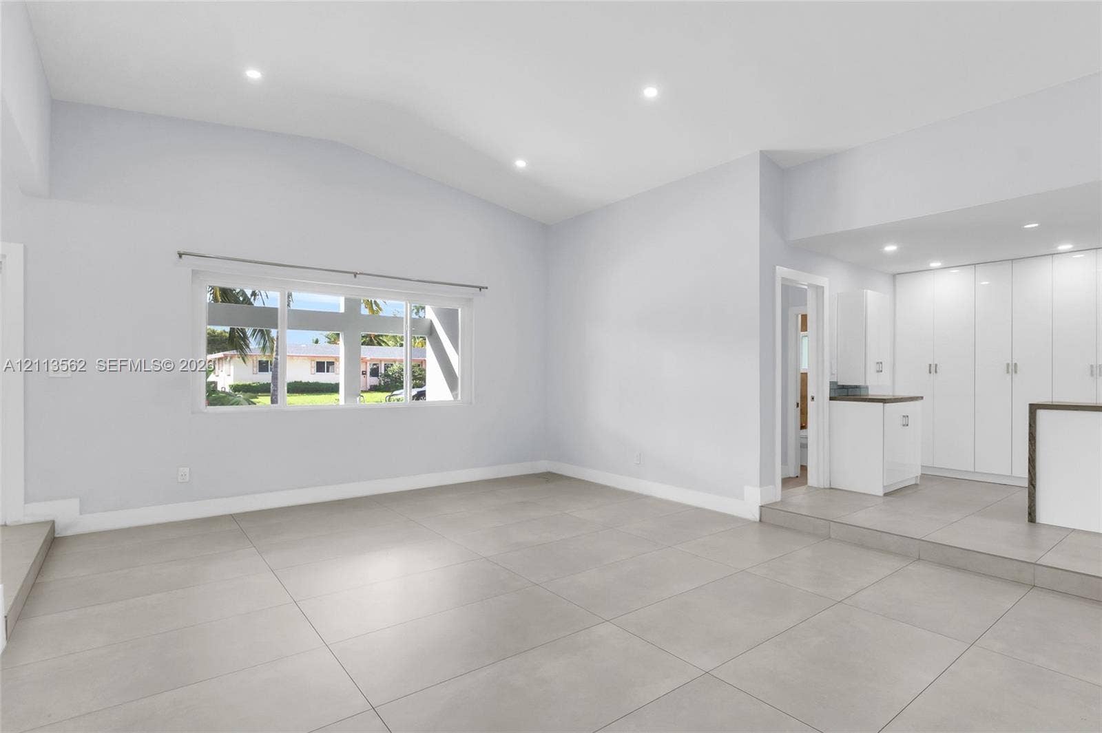 Open-concept space featuring vaulted ceilings, large-format tile flooring, recessed lighting, and built-in white cabinetry with a dedicated countertop surface