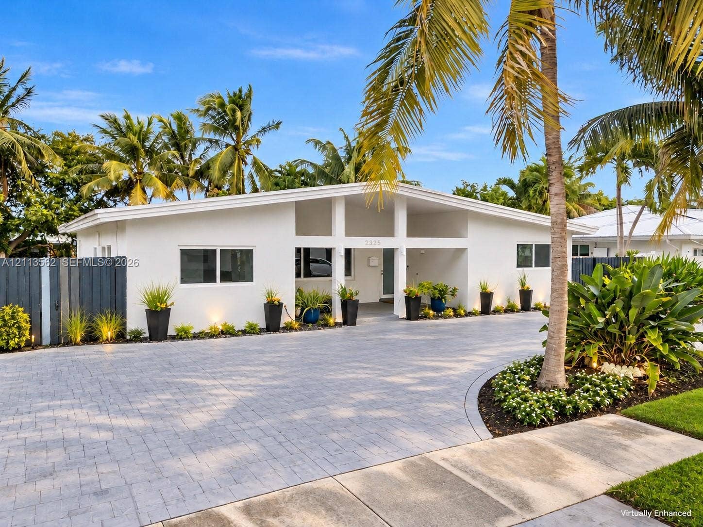 Mid-century modern exterior featuring a low-pitched roofline, structural portico, paver-stone driveway, and clean white facade