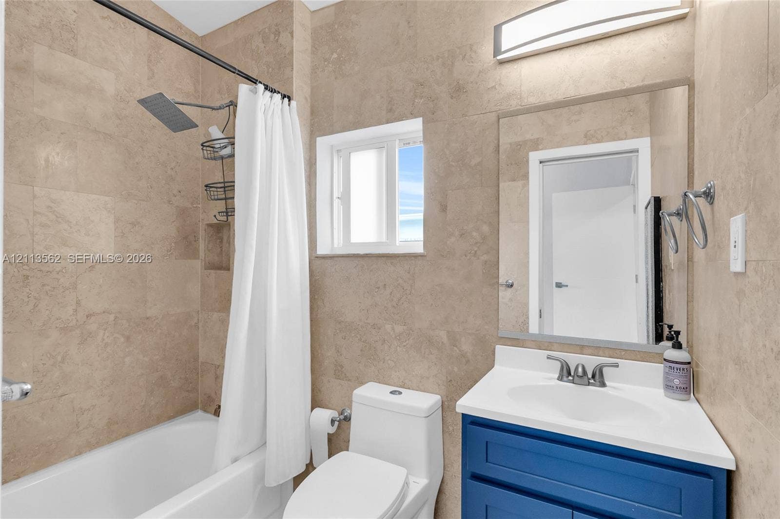 Full-height stone tile wall surround, blue vanity with white countertop, rectangular undermount sink, rainfall showerhead, and integrated wall-mounted lighting