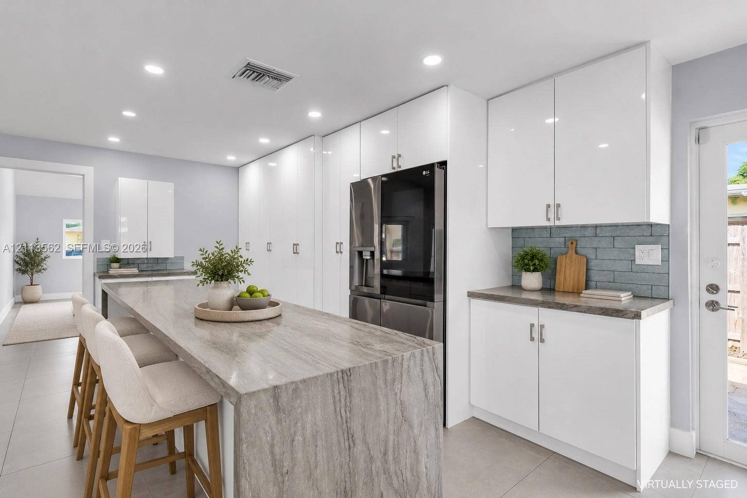 Kitchen featuring high-gloss white cabinetry, waterfall-edge stone island, gray subway tile backsplash, and recessed lighting