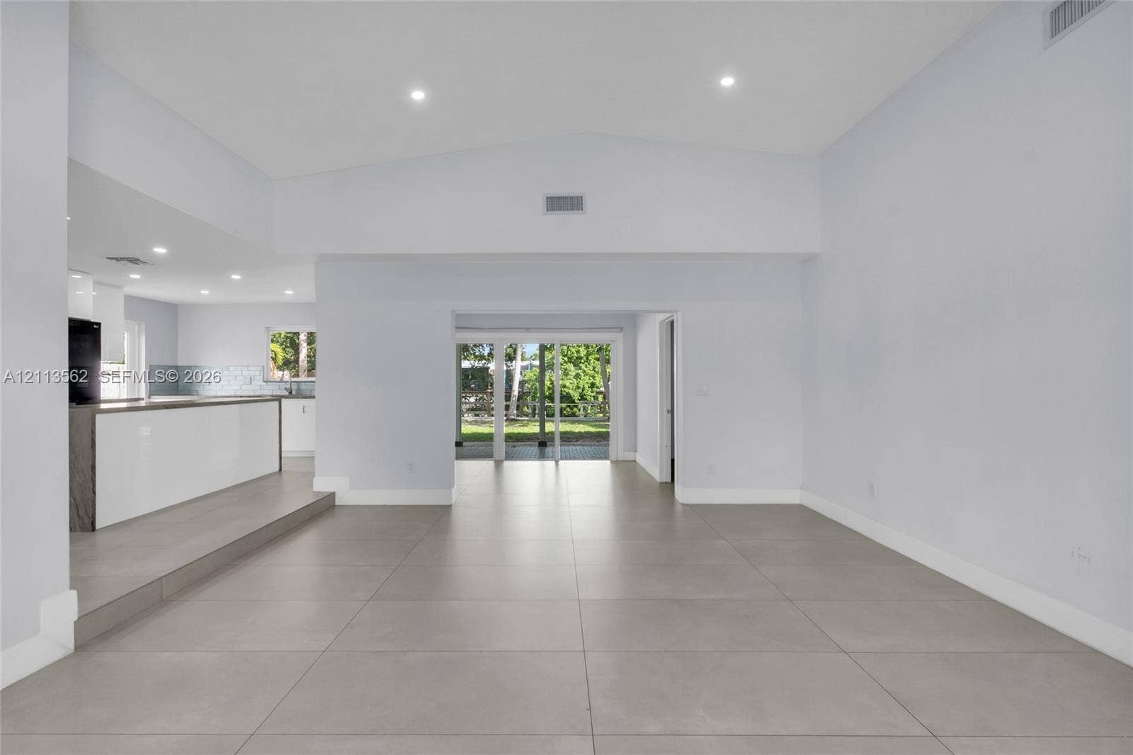 Open-concept interior featuring large-format tile flooring, vaulted ceilings, recessed lighting, and sliding glass doors