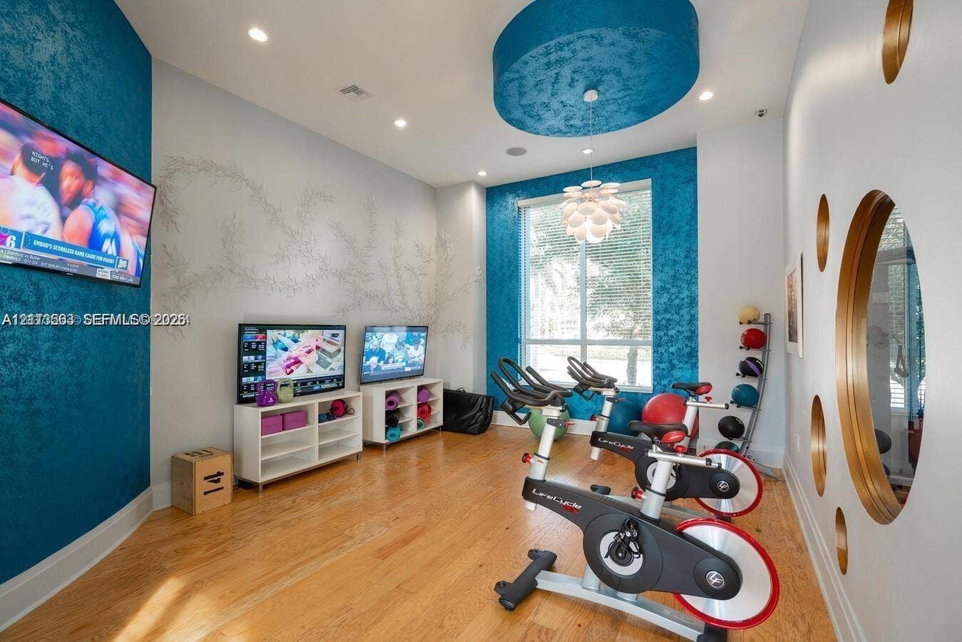 320 Franklin Club Drive, #Boynton, Delray Beach, Delray Beach, FL 33483 Room featuring wood-finish flooring, textured teal accent walls, a circular recessed ceiling detail with a tiered light fixture, large window, and wall-integrated circular glass accents