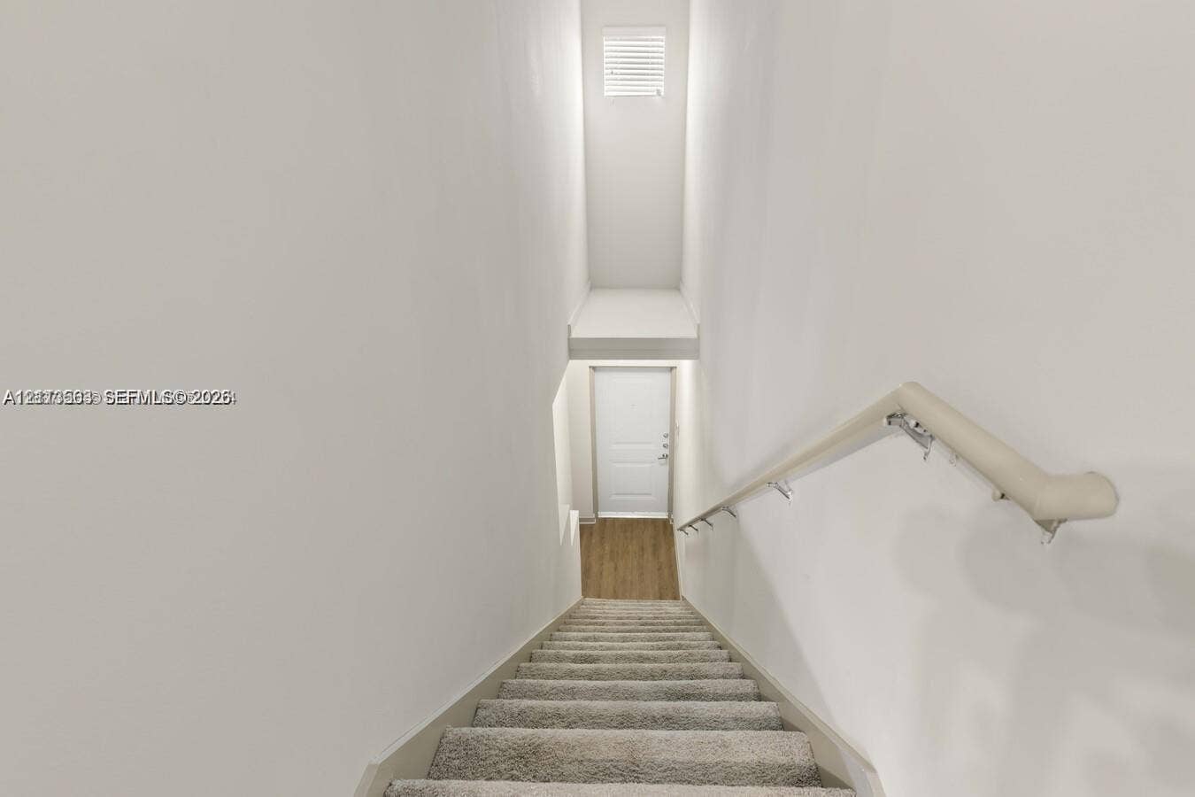 320 Franklin Club Drive, #Boynton, Delray Beach, Delray Beach, FL 33483 Staircase featuring neutral-toned carpeting, a wall-mounted handrail, and a direct line of sight to a white interior door with wood-finish flooring