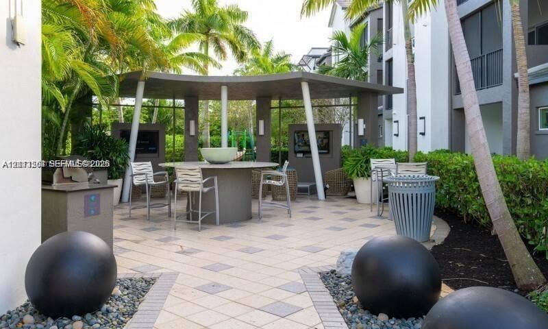 320 Franklin Club Drive, #Boynton, Delray Beach, Delray Beach, FL 33483 Covered outdoor pavilion with a central stone-topped table and built-in wall displays, surrounded by tile hardscaping, decorative stone spheres, and lush landscaping