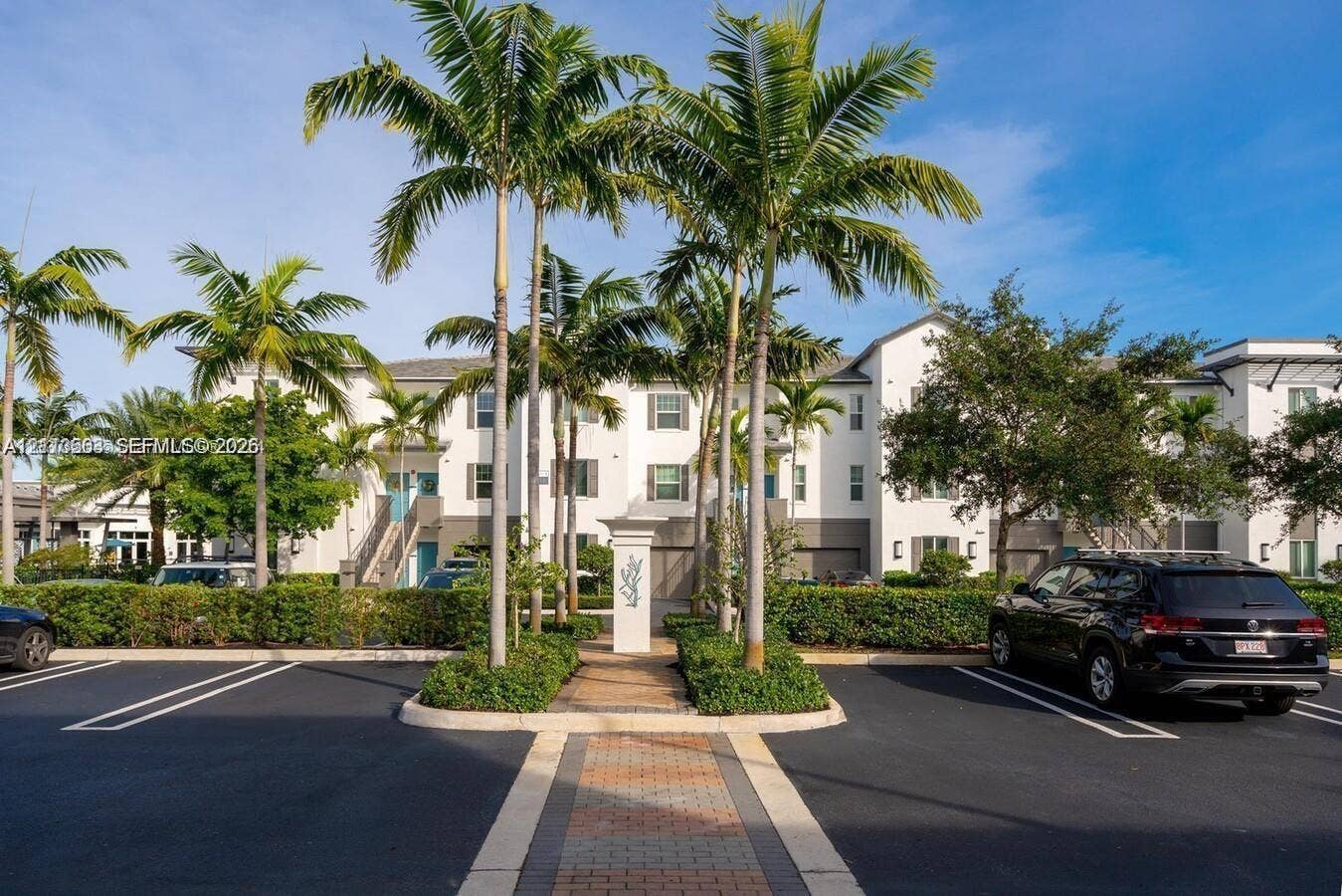 320 Franklin Club Drive, #Boynton, Delray Beach, Delray Beach, FL 33483 Multi-story building exterior with white and gray stucco facade, paved pedestrian walkway, manicured hedging, and mature palm landscaping