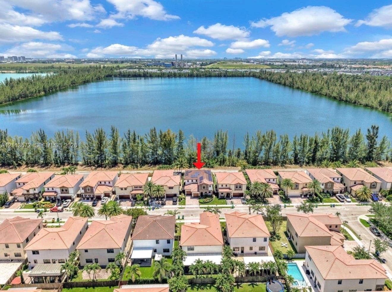 9860 NW 86th Terrace, Doral, FL 33178 Aerial perspective featuring a two-story residence with a multi-hipped roof, positioned along a waterfront bordered by mature trees