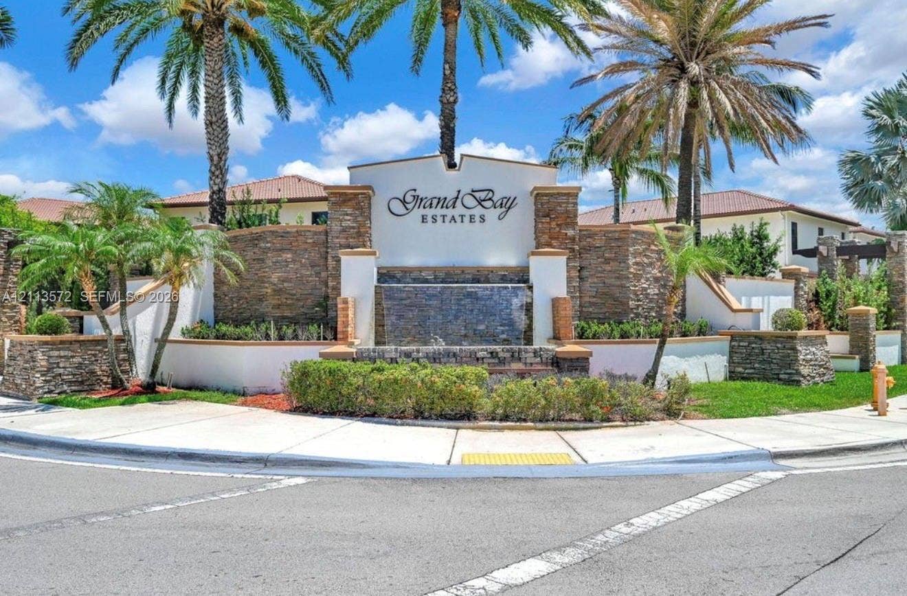 9860 NW 86th Terrace, Doral, FL 33178 Community entrance featuring stacked-stone masonry, a built-in water feature, manicured landscaping, and mature palm trees