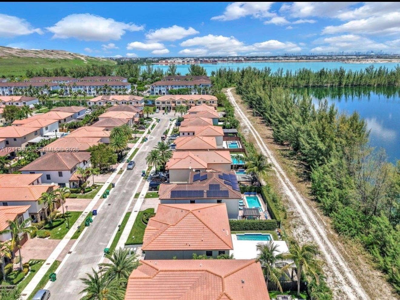 9860 NW 86th Terrace, Doral, FL 33178 Aerial perspective of residential neighborhood featuring tile-roofed structures, solar panel arrays, private swimming pools, and waterfront placement