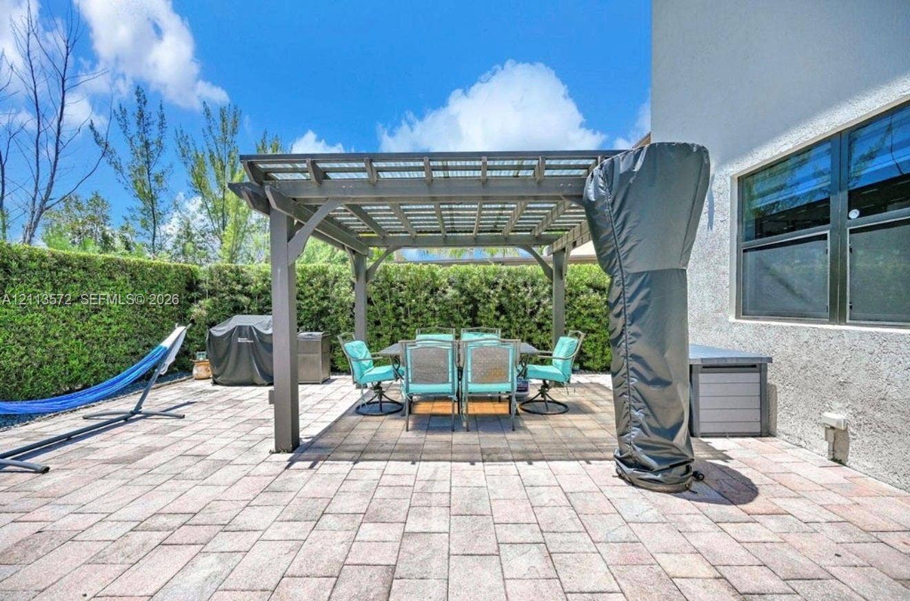 9860 NW 86th Terrace, Doral, FL 33178 Outdoor patio area featuring a stone-paver surface, a fixed pergola, and a tall privacy hedge