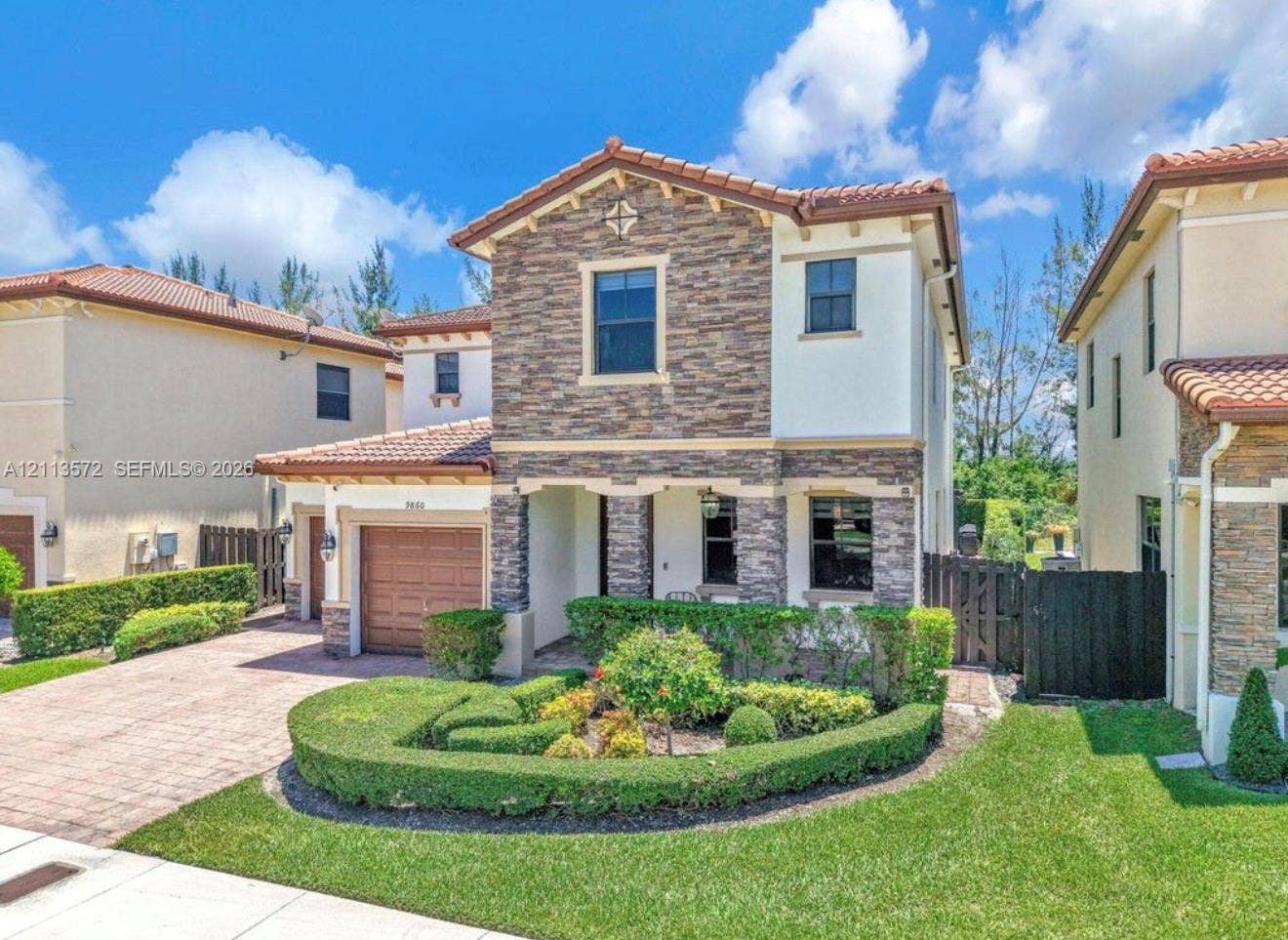 9860 NW 86th Terrace, Doral, FL 33178 Two-story residence featuring a tile roof, decorative stone veneer faade, manicured landscaping, and a paved driveway
