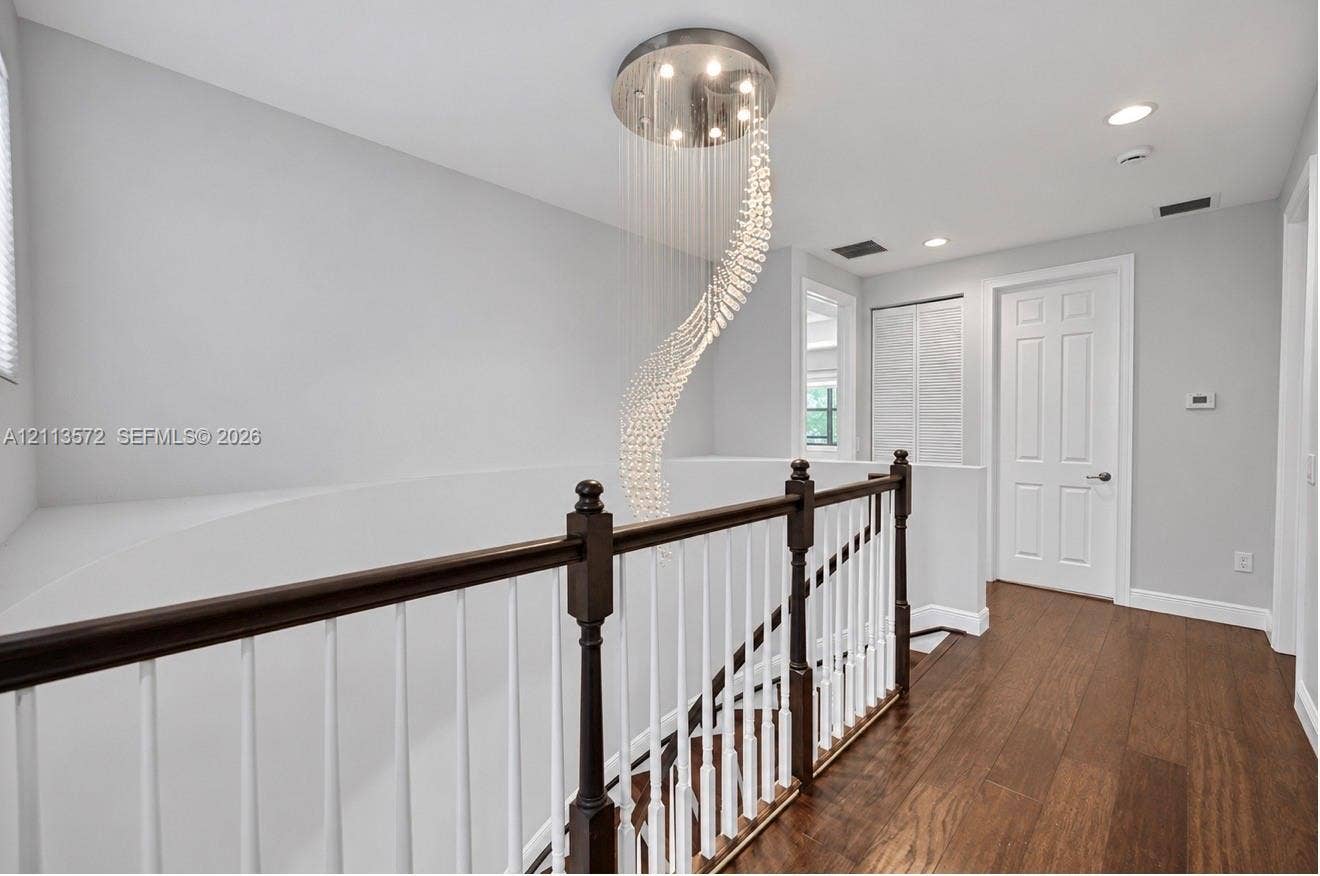 9860 NW 86th Terrace, Doral, FL 33178 Spiral crystal chandelier with recessed ceiling lighting, wood-finish flooring, and a two-tone railing featuring a dark wood handrail and white balusters