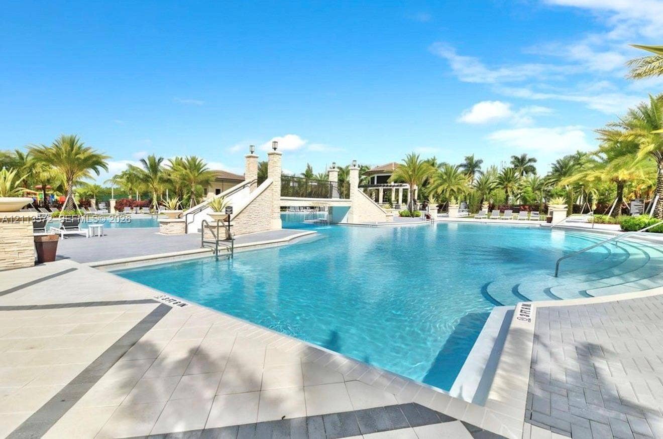 9860 NW 86th Terrace, Doral, FL 33178 Expansive swimming pool featuring a decorative pedestrian bridge, stone-finish columns, tiered entry steps, and paved surround