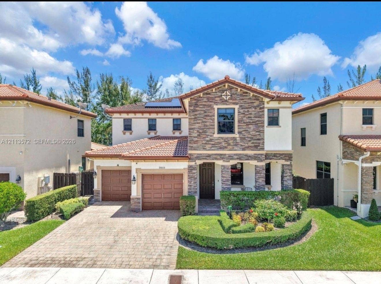 9860 NW 86th Terrace, Doral, FL 33178 Two-story exterior featuring a stone facade, tile roof, dual-car garage, solar panels, and a paved driveway