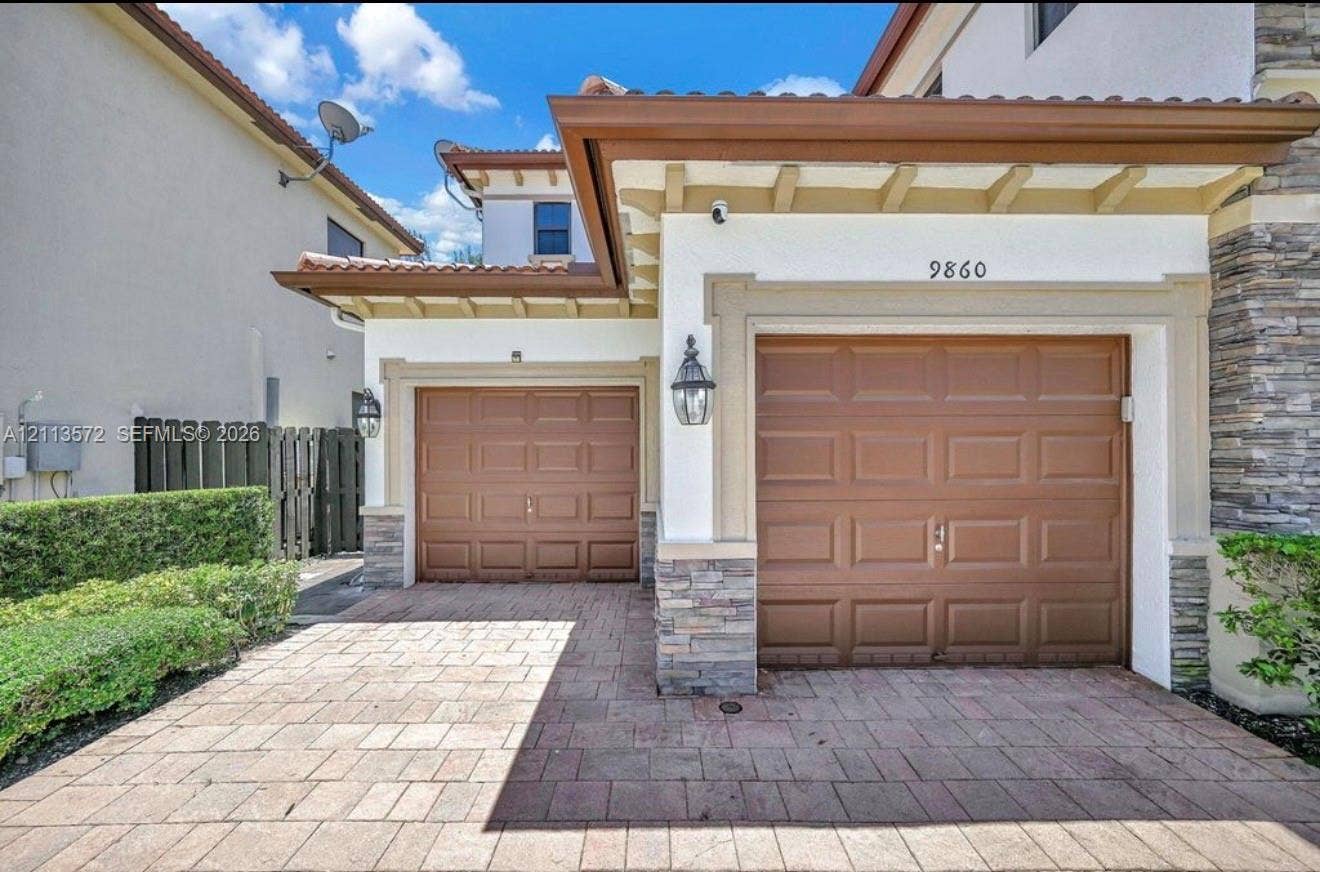9860 NW 86th Terrace, Doral, FL 33178 Stucco exterior with stone veneer accents, dual-car garage with paneled doors, and paved driveway