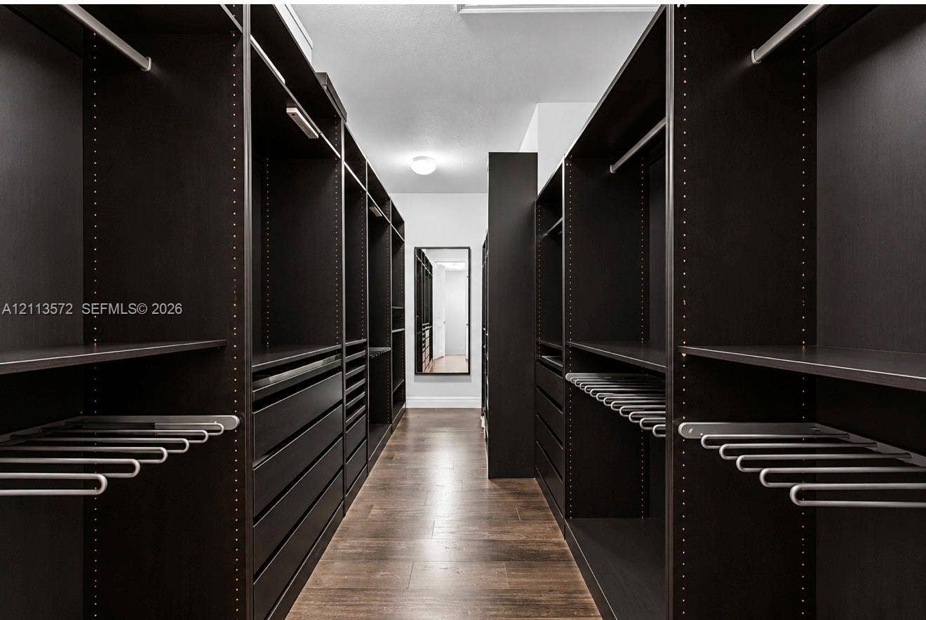 9860 NW 86th Terrace, Doral, FL 33178 Custom walk-in storage featuring dark-finish cabinetry, built-in shelving, integrated pull-out drawers, metal garment rods, and wood-finish flooring