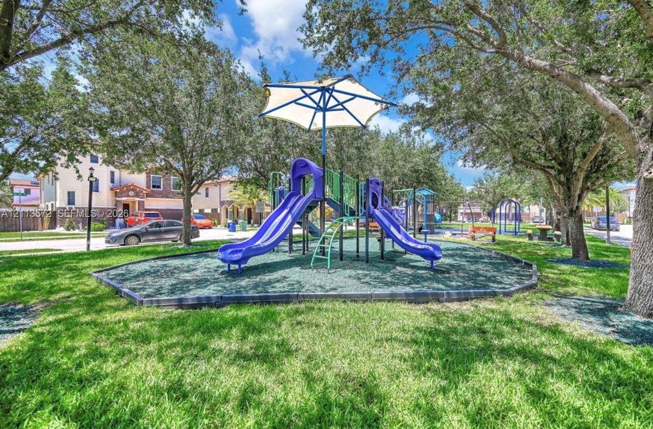 9860 NW 86th Terrace, Doral, FL 33178 Community park featuring a central playground structure with dual slides, a canopy cover, manicured lawn, and mature canopy trees