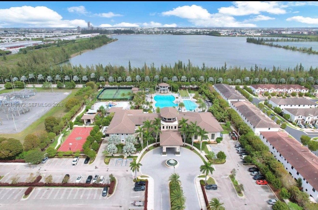 9860 NW 86th Terrace, Doral, FL 33178 Aerial perspective of the community center featuring a swimming pool, tennis court, basketball court, and central fountain, situated alongside a lake