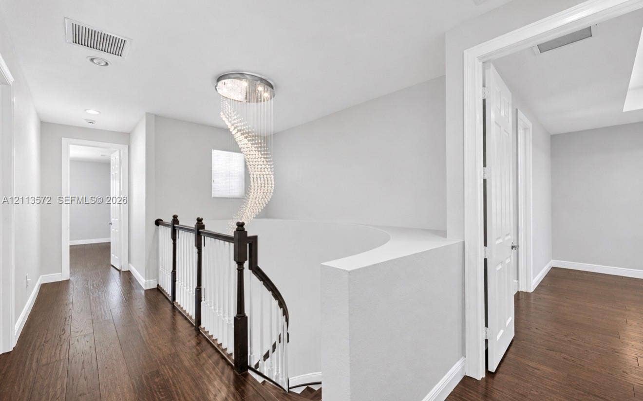 9860 NW 86th Terrace, Doral, FL 33178 Spiral crystal chandelier, wood-finish flooring, and curved staircase railing featuring dark wood handrails with white balusters