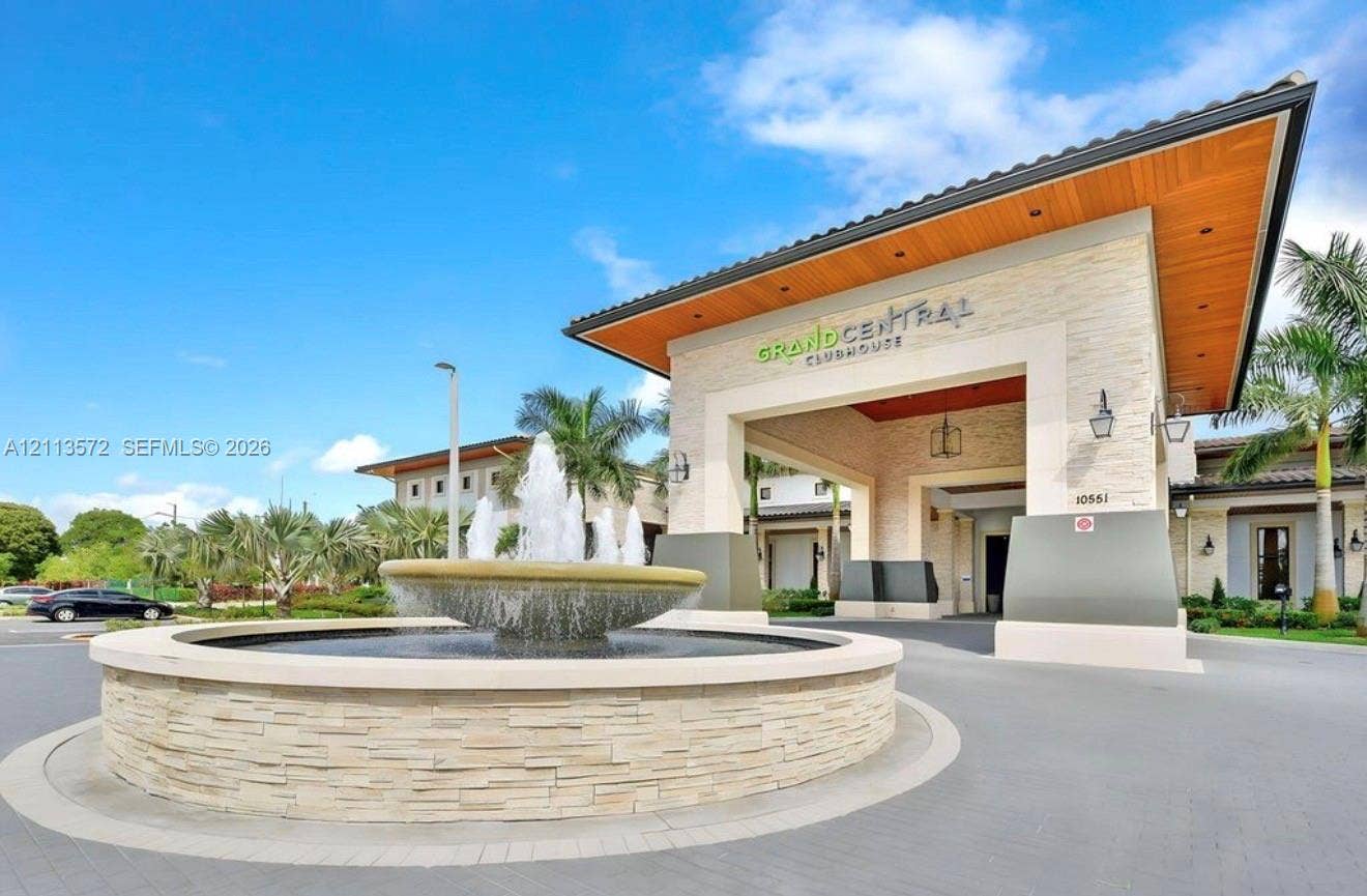 9860 NW 86th Terrace, Doral, FL 33178 Grand Central clubhouse exterior featuring a stone-clad portico, wood-finish ceiling under the eave, paver driveway, and a central tiered stone fountain