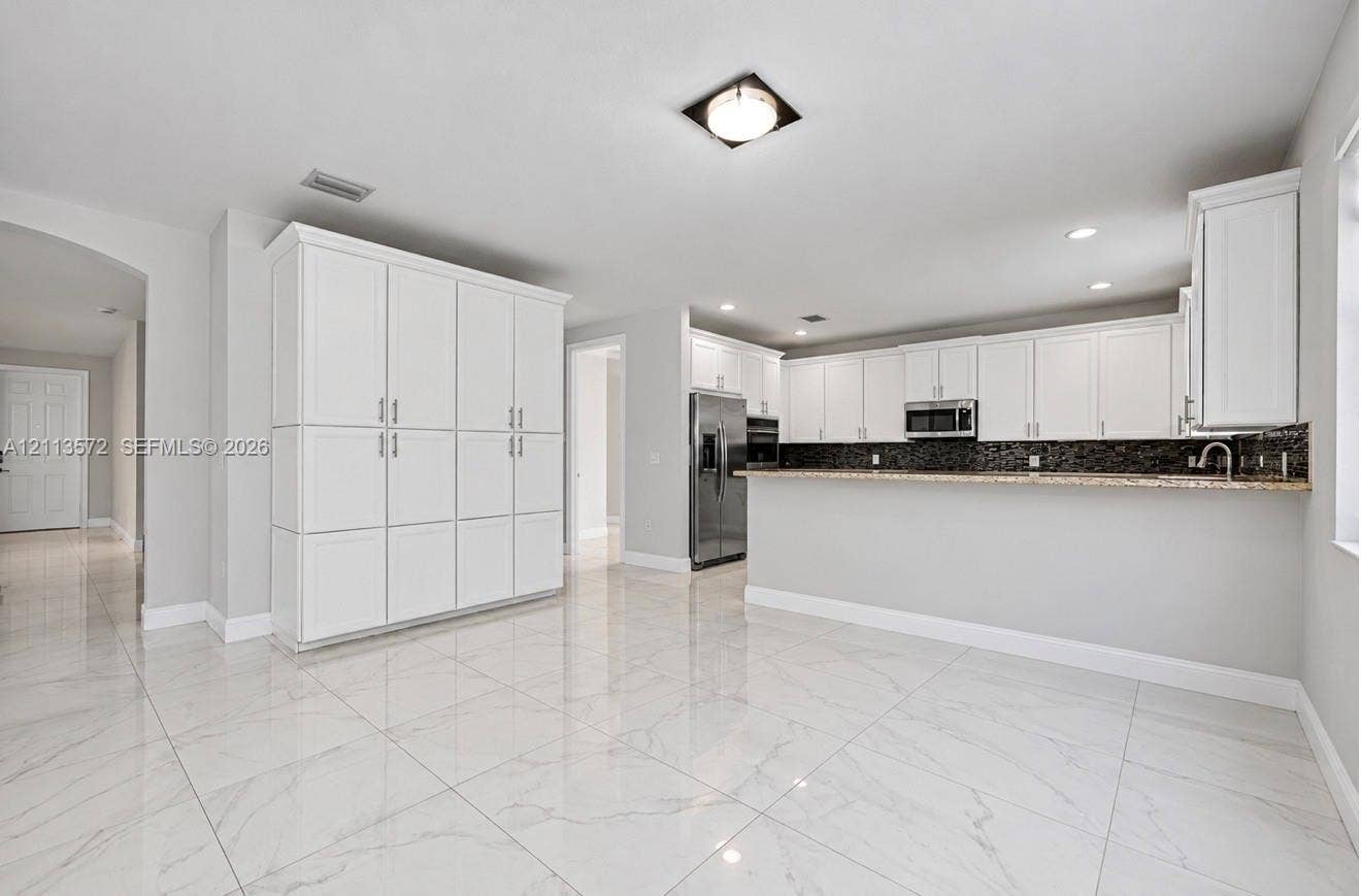 9860 NW 86th Terrace, Doral, FL 33178 Kitchen featuring white shaker-style cabinetry, a stone-patterned breakfast bar, stainless steel appliances, and large-format porcelain tile flooring