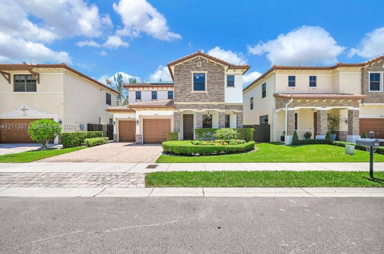 9860 NW 86th Terrace, Doral, FL 33178 Two-story residence featuring a stone-veneer faade, clay tile roof, dual-car garage, and a manicured front lawn