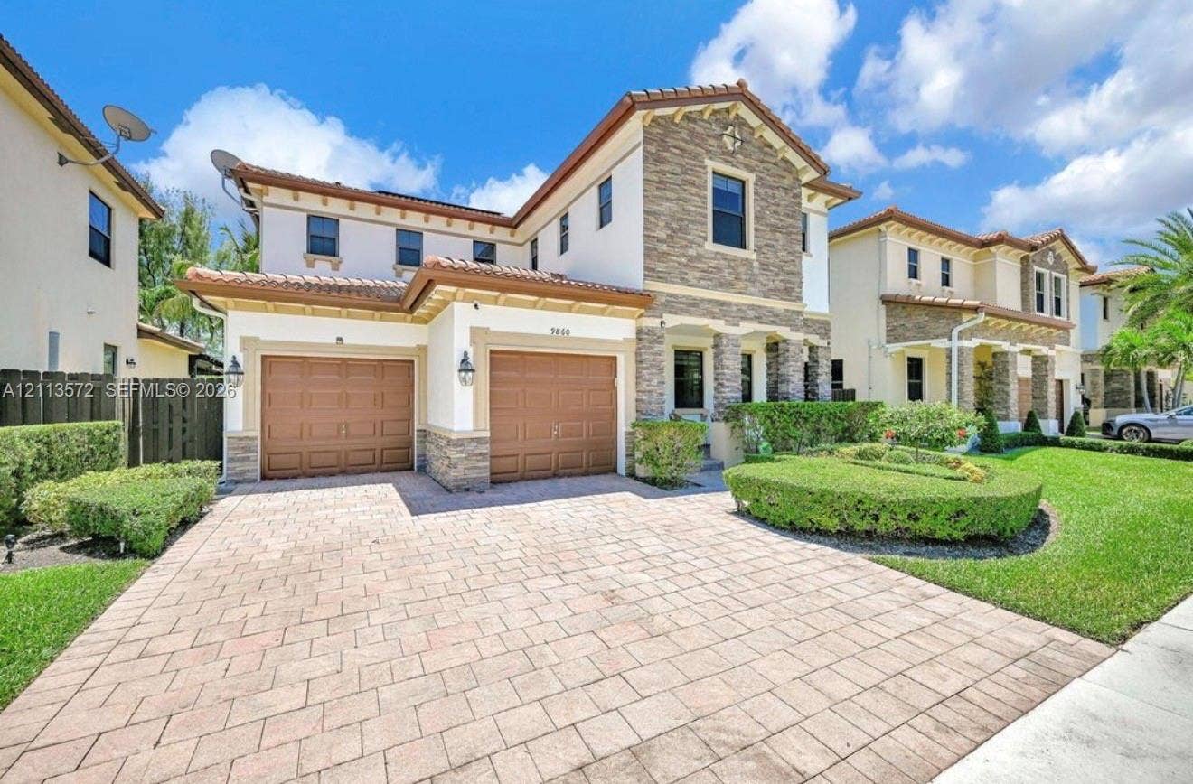9860 NW 86th Terrace, Doral, FL 33178 Two-story residence featuring a stone veneer facade, paver driveway, two-car garage, and manicured landscaping
