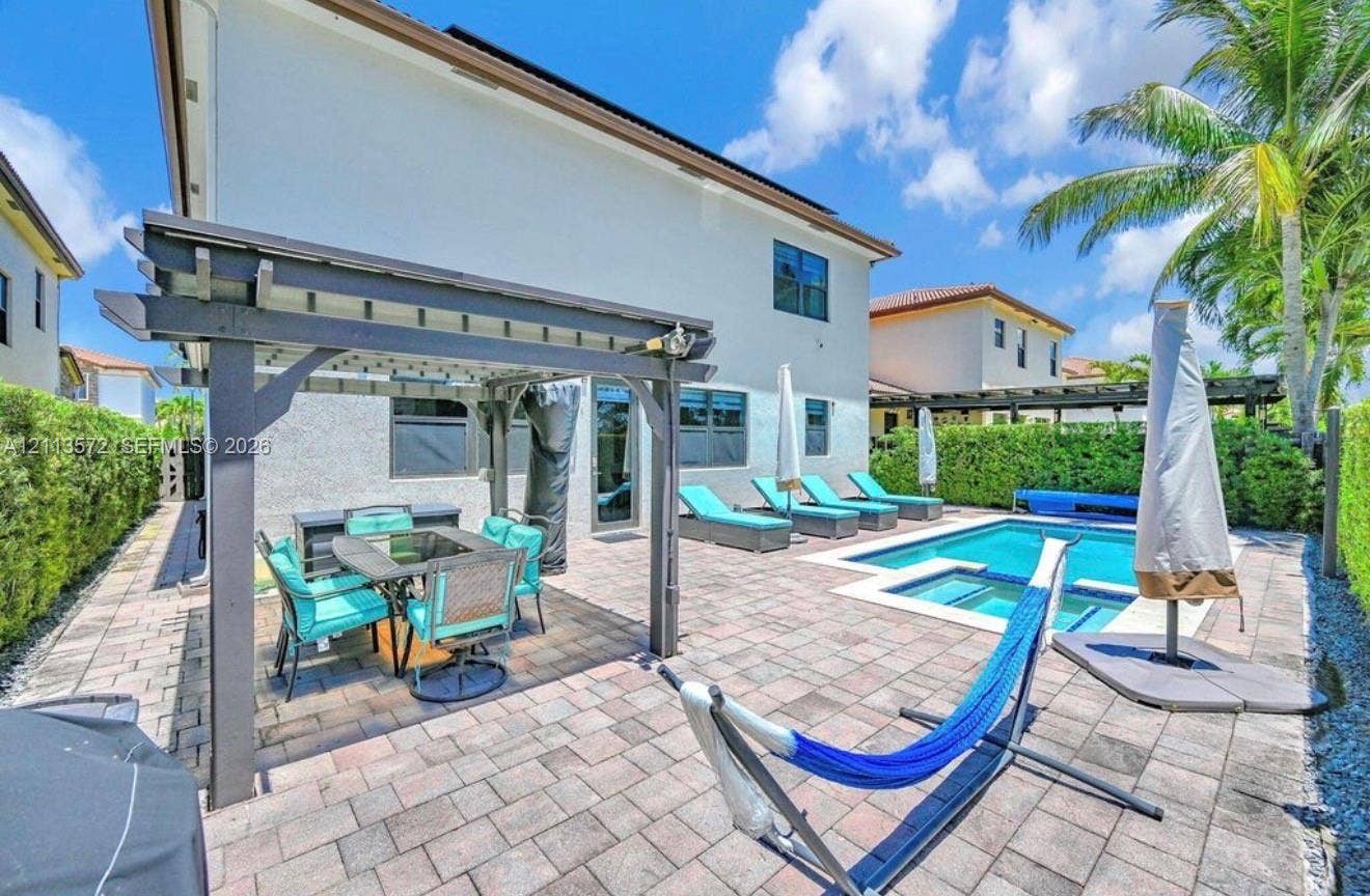 9860 NW 86th Terrace, Doral, FL 33178 Outdoor living space featuring a paved stone patio, covered pergola, in-ground swimming pool, integrated spa, and perimeter privacy hedges
