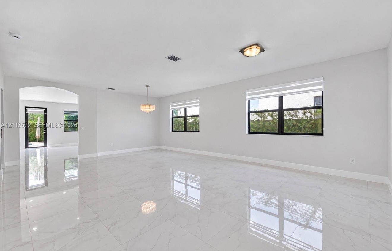 9860 NW 86th Terrace, Doral, FL 33178 Open-concept interior featuring large-format polished tile flooring, black-framed windows, a multi-light chandelier, and an arched entryway