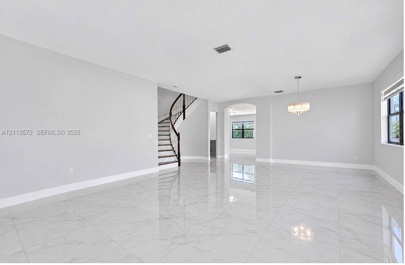 9860 NW 86th Terrace, Doral, FL 33178 Open-concept interior featuring large-format polished stone-finish flooring, a curved staircase with a dark wood handrail, an arched entryway, and a tiered drum chandelier