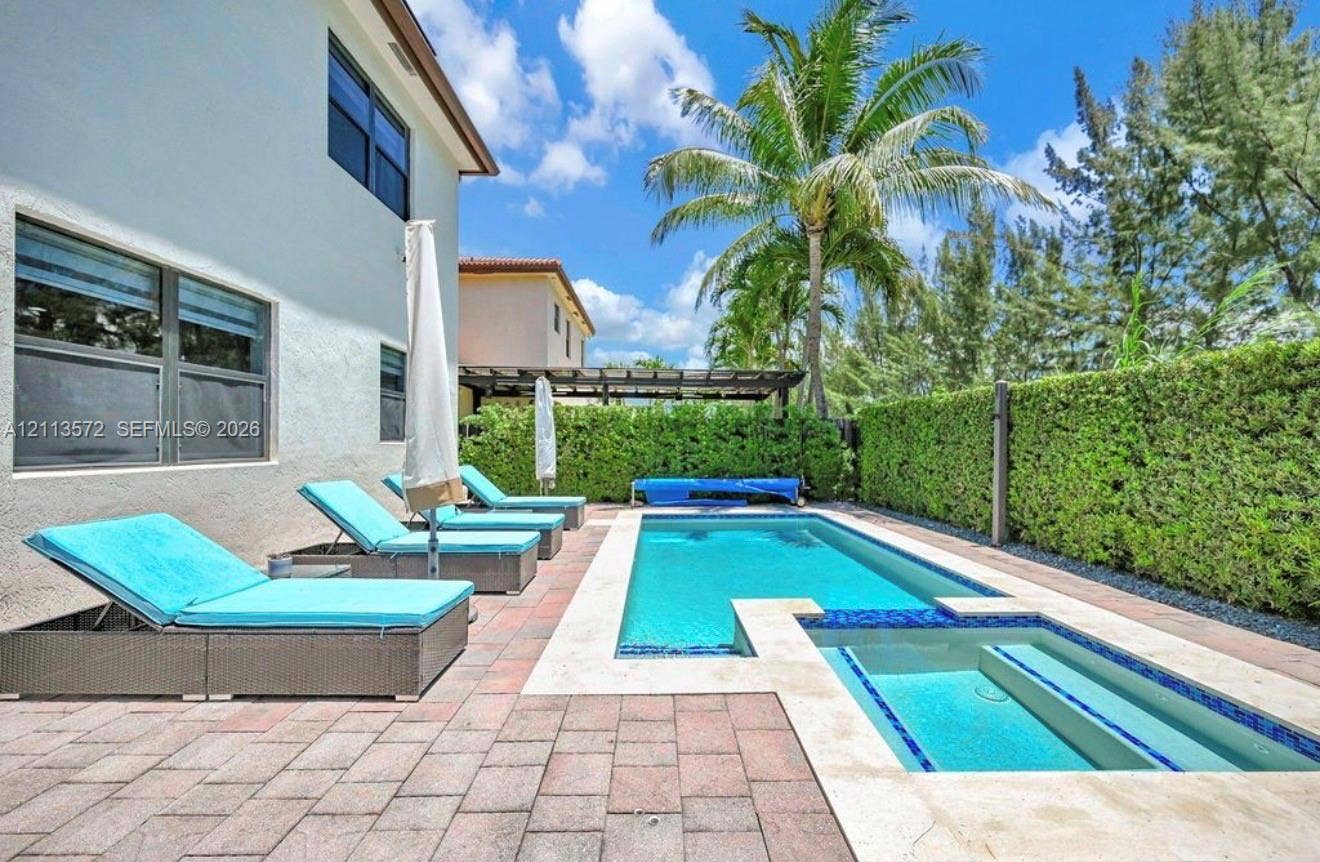 9860 NW 86th Terrace, Doral, FL 33178 Rear patio featuring a swimming pool with integrated spa, paver hardscaping, and privacy hedges