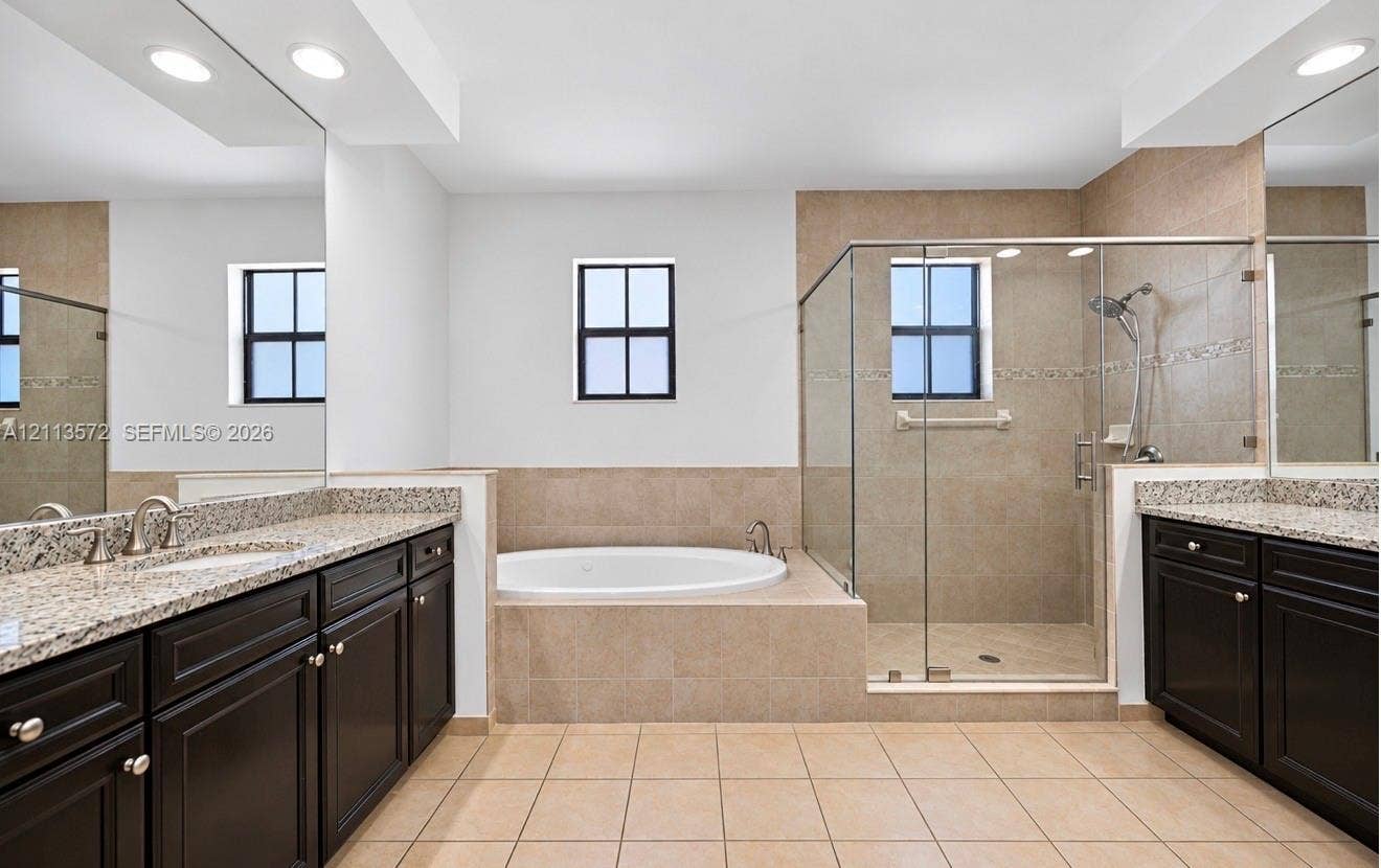 9860 NW 86th Terrace, Doral, FL 33178 Dual vanities with stone countertops and dark cabinetry, large soaking tub with tile surround, and walk-in glass-enclosed shower with tiled walls