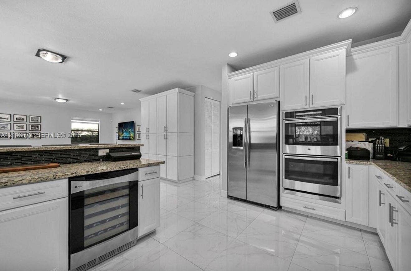 9860 NW 86th Terrace, Doral, FL 33178 Kitchen featuring white shaker-style cabinetry, stainless steel side-by-side refrigerator, built-in double wall oven, integrated wine refrigerator, and stone countertops