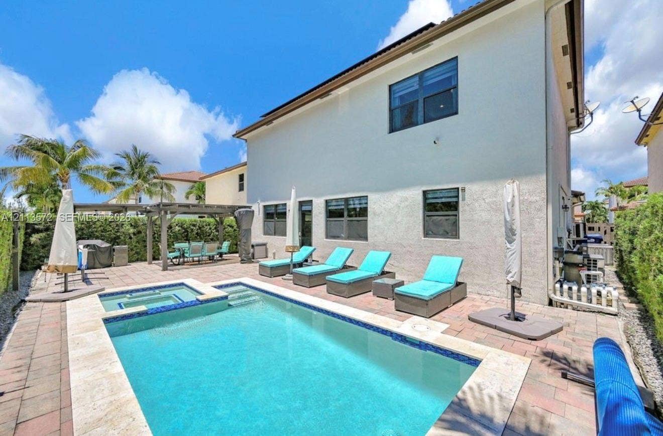 9860 NW 86th Terrace, Doral, FL 33178 In-ground pool with integrated spa, stone-paver pool deck, and wood-framed pergola