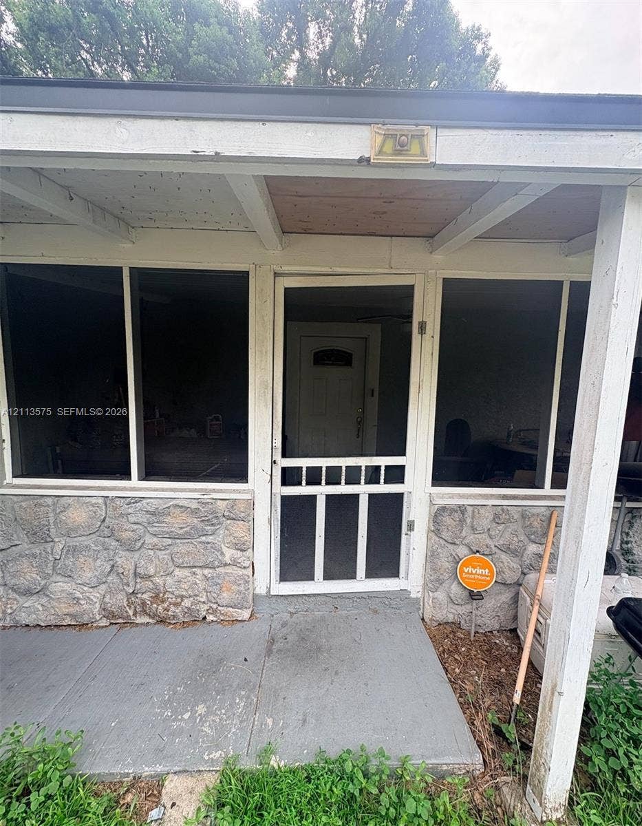 10009 Morris Bridge Road, Tampa, FL 33637 Covered porch featuring stone masonry foundation, large glass pane windows, and a white screen door