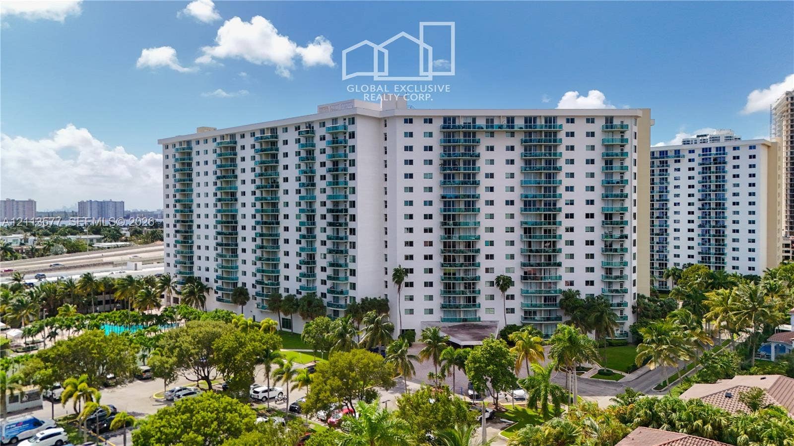 19370 Collins Avenue, #1622, Sunny Isles Beach, FL 33160 High-rise residential building featuring stacked private balconies with glass railings, an exterior swimming pool, mature palm tree landscaping, and paved parking areas