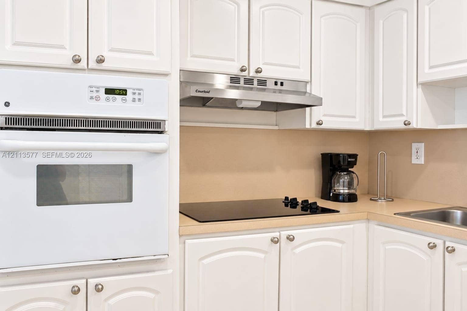 19370 Collins Avenue, #1622, Sunny Isles Beach, FL 33160 Kitchen featuring white raised-panel cabinetry, built-in white wall oven, stainless steel range hood, smooth-top electric cooktop, and solid-surface countertops