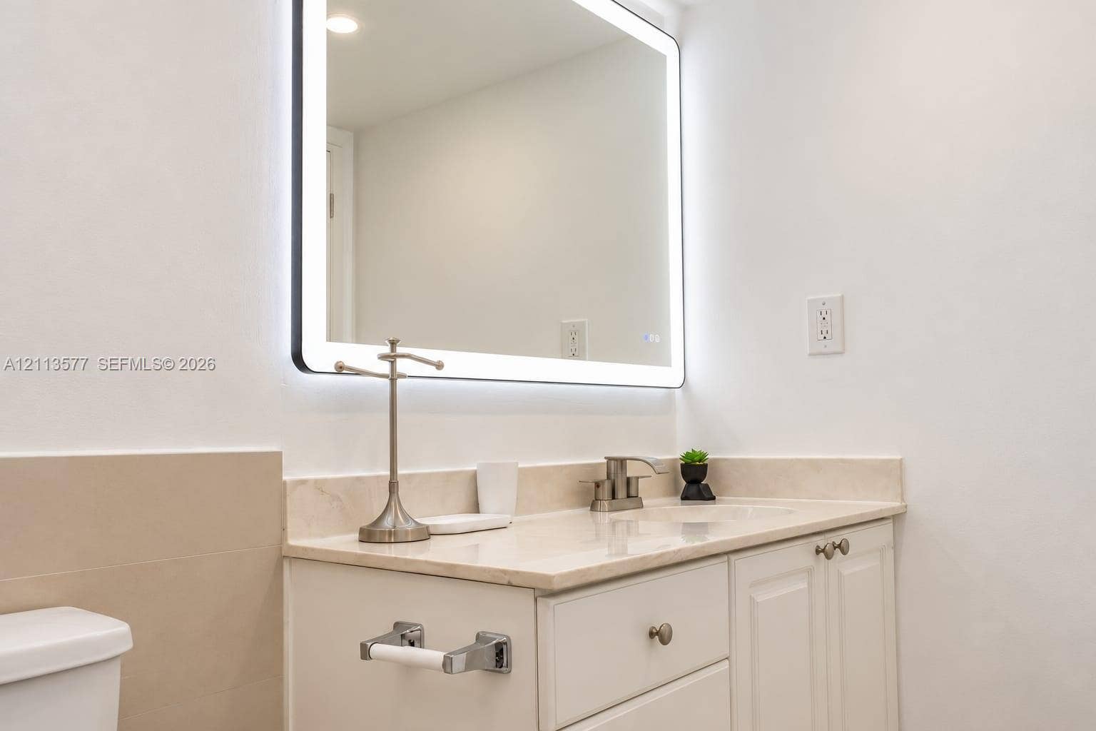 19370 Collins Avenue, #1622, Sunny Isles Beach, FL 33160 Rectangular LED-backlit mirror featuring rounded corners, paired with a white vanity cabinet, solid-surface countertop with integrated basin, and brushed-finish faucet