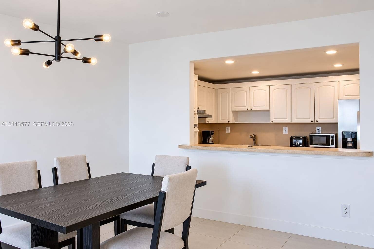 19370 Collins Avenue, #1622, Sunny Isles Beach, FL 33160 Modern black metal sputnik chandelier, white cabinetry, solid-surface breakfast bar, recessed lighting, and tile flooring