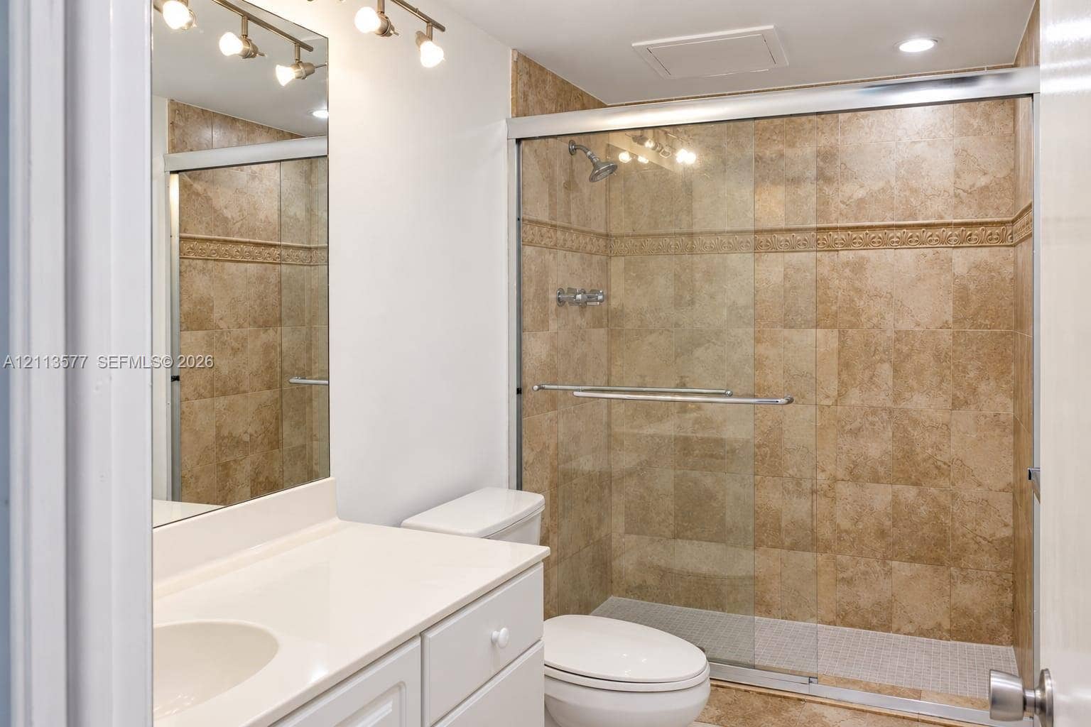 19370 Collins Avenue, #1622, Sunny Isles Beach, FL 33160 Bathroom featuring a vanity with a white countertop, an integrated sink, a full-length wall mirror, multi-light fixture, and a shower enclosure with floor-to-ceiling stone-finish tile surround and sliding glass doors