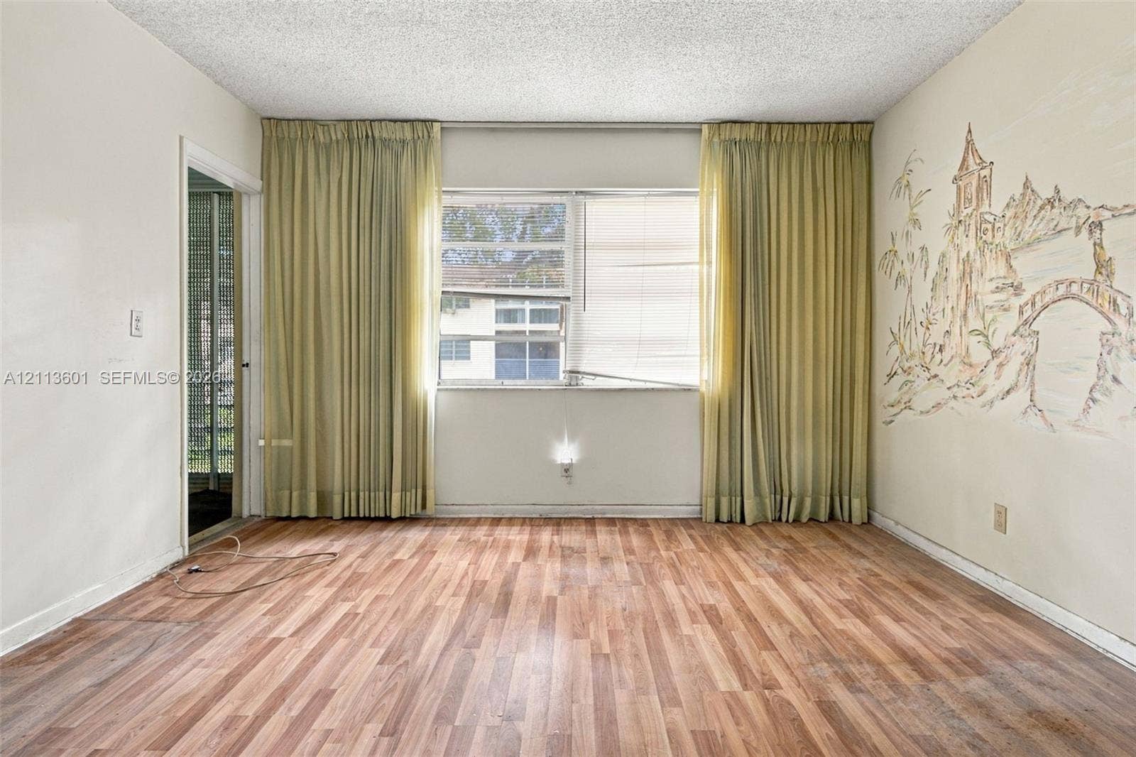 Room featuring wood-finish flooring, a large window with neutral drapery, and a textured ceiling