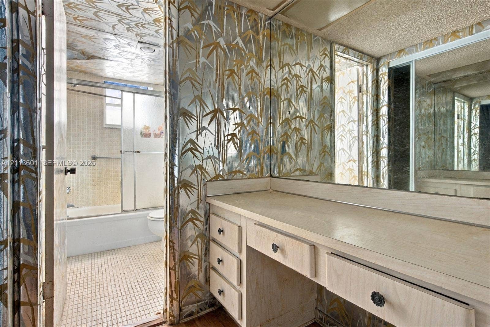 Built-in light-colored wood vanity featuring multiple storage drawers, full-width wall mirror, and metallic patterned wall covering