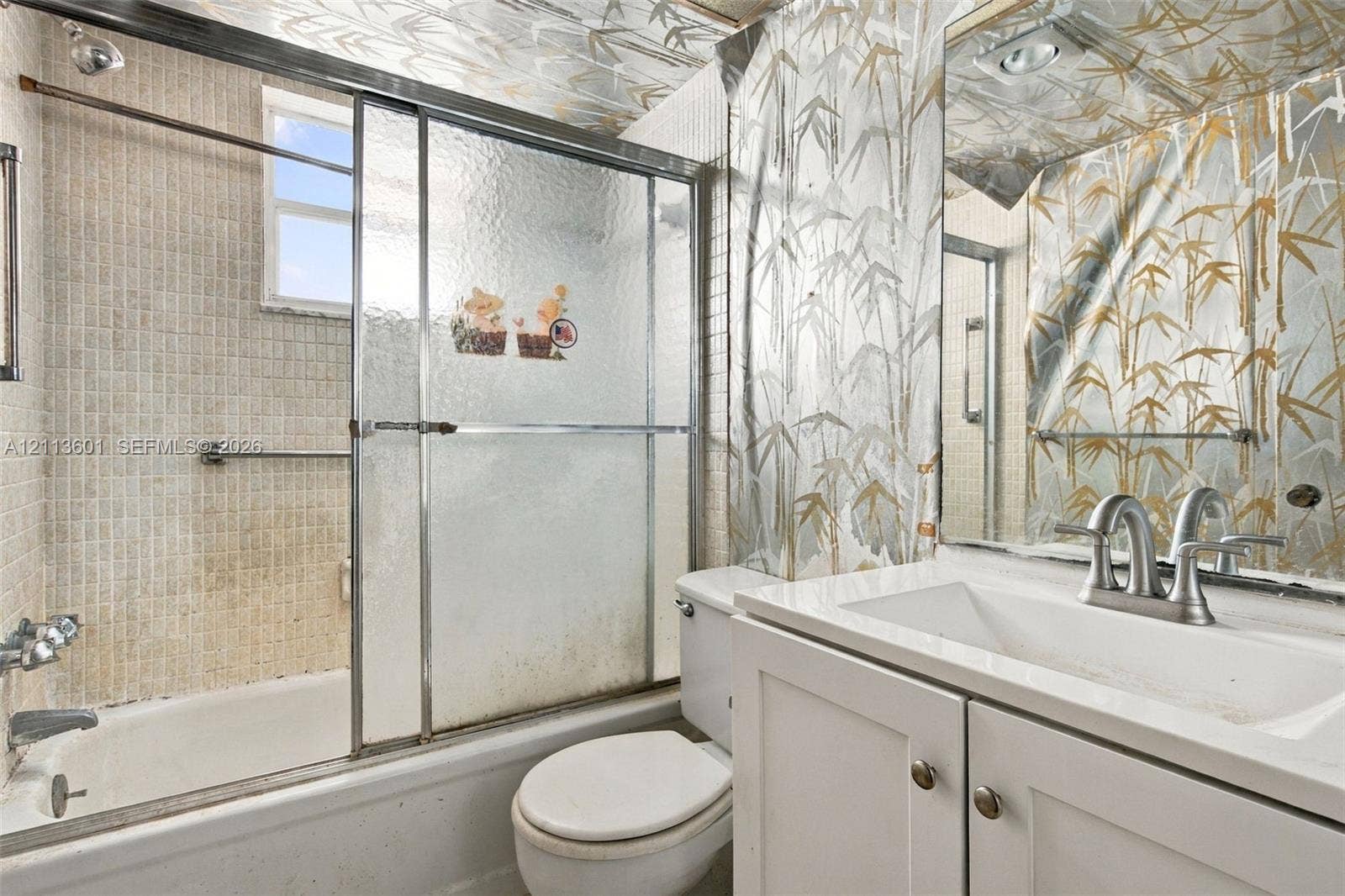 Bathroom featuring a vanity with an integrated countertop sink, chrome-finish faucet, sliding glass shower doors, and a tiled tub surround